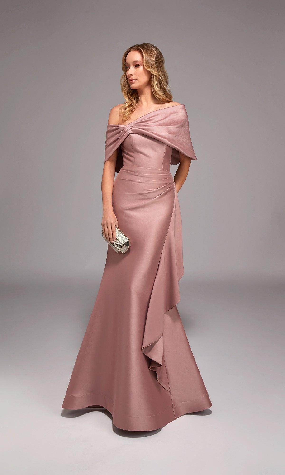 A woman in a rosewood Alyce 27822 long formal dress with an off-the-shoulder, floor-length mermaid silhouette holds a small silver clutch against a plain gray backdrop.